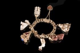 PULSERA Realizada en oro de 18 kt., tipo doble húngara, de la que penden siete colgantes: un buda, dos perros (uno deteriorado), un busto egipcio, un colgante piramidal con piedras de color, un corazón y los tres monos sabios. Cierre con ocho y cadenilla