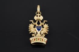 COLGANTE Realizado en oro y pequeña pieza de metal, representando el escudo del Imperio Austriaco formado por un águila bicéfala tocada con una corona, que sostiene en sus patas un orbe y una espada flameante; en el centro sobre esmalte la F, en referenci