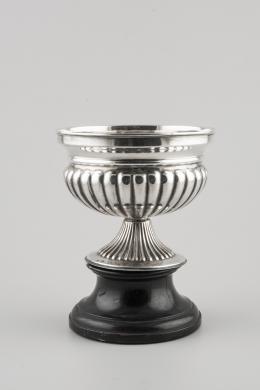 TROFEO Realizado en plata en su color, en forma de copa, con fuste y depósito gallonados. Apoya sobre peana de madera. Contraste: estrella de cinco puntas.