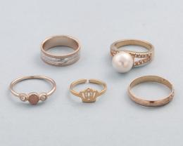 LOTE DE 5 ANILLOS DE METAL DORADO. conjunto de cinco anilos de metal dorado, un anillo bicolor, dos con piedras incoloras y una perla y un anillo con motivo de corona.