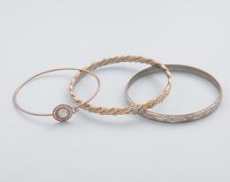 LOTE DE TRES PULSERAS RÍGIDAS EN METAL DORADO. conjunto de tres pulseras rígidas en metal dorado, pulsera con piedra incolora y cierre, pulsera con decoración en forma de cadena (presenta deterioro) y una pulsera bicolor. 